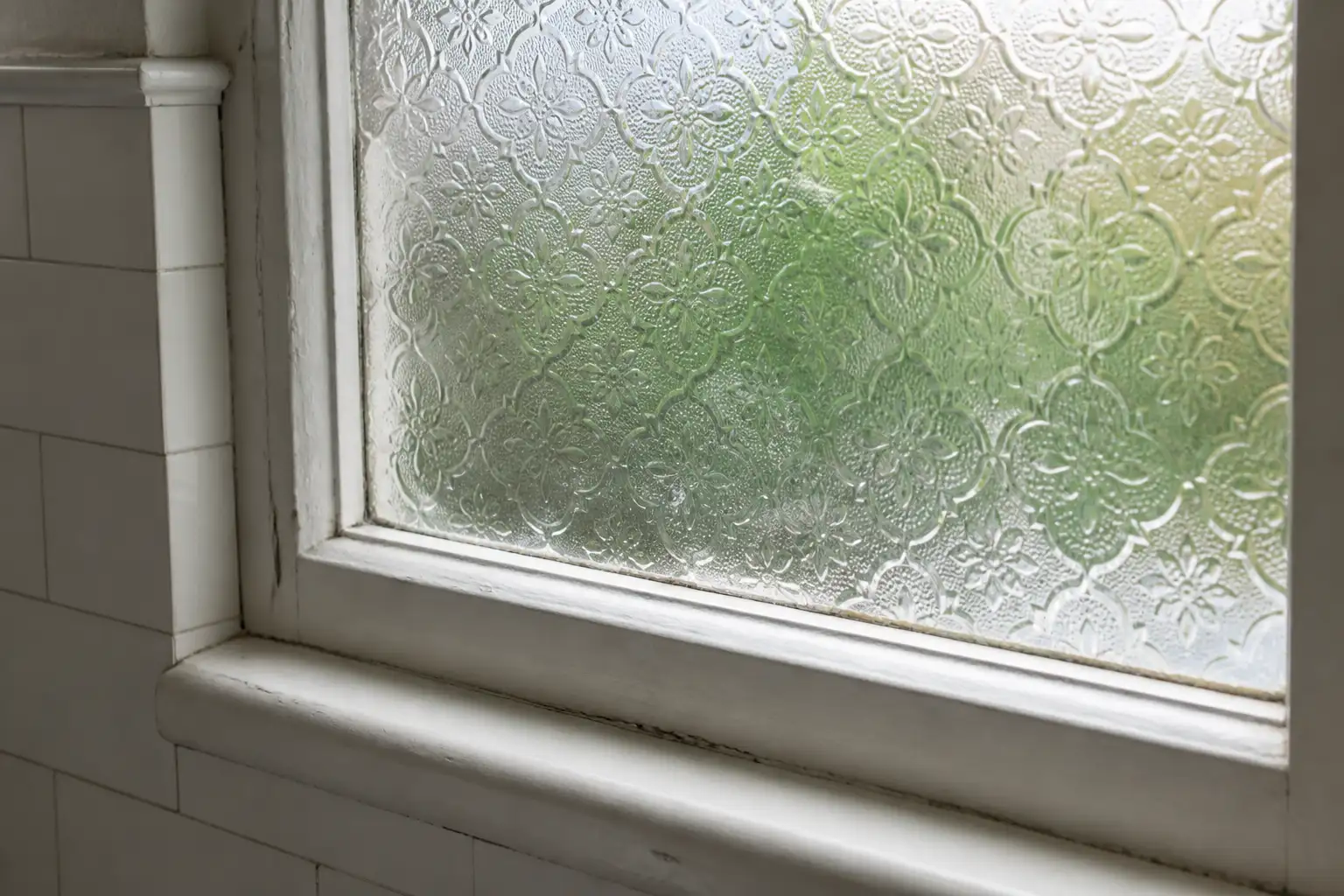 Altes Badezimmerfenster mit strukturiertem Ornamentglas, auf dem Fensterfolie nicht haftet