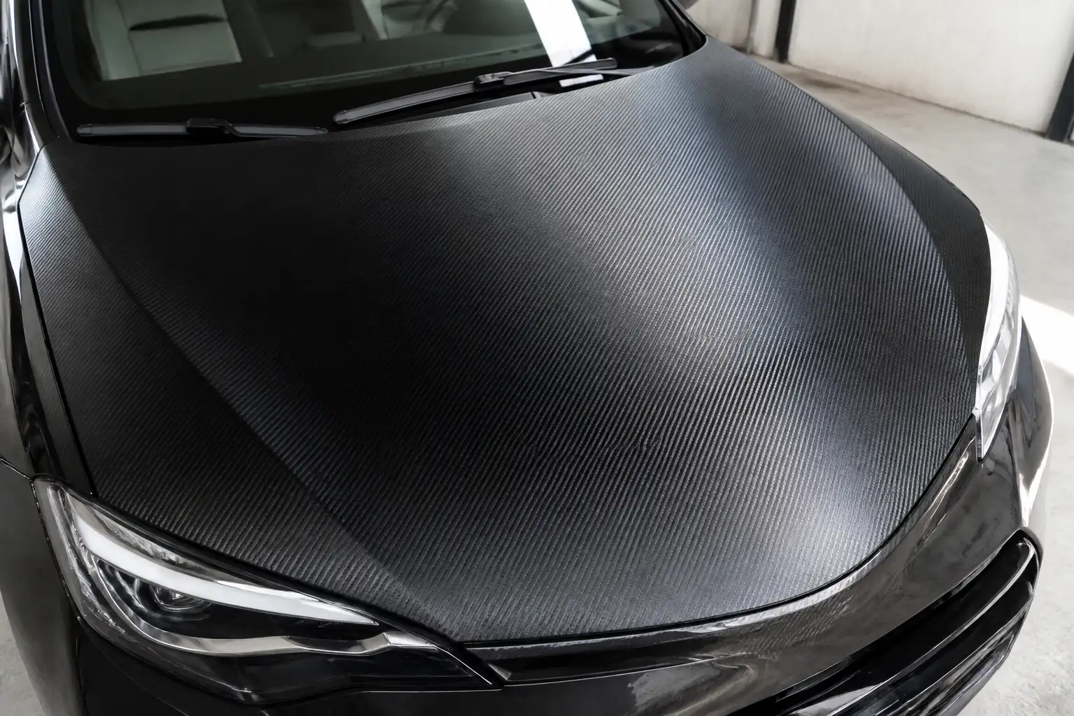 Motorhaube eines Autos, vollständig mit schwarzer Folie in Carbon-Optik beklebt