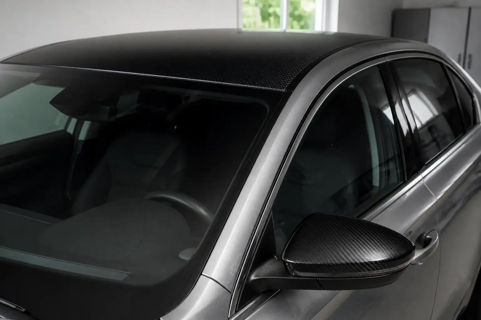 Silbergrauer Pkw in einer hellen Garage, Dach und Außenspiegelkappe sauber mit schwarzer Carbonfolie beklebt